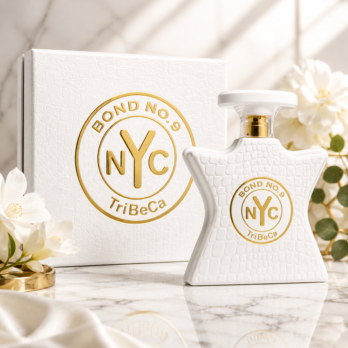 A white textured perfume bottle with a gold and white 'Bond No. 9 NYC TriBeCa' logo, displayed next to its matching white textured box on a marble surface with white flowers.