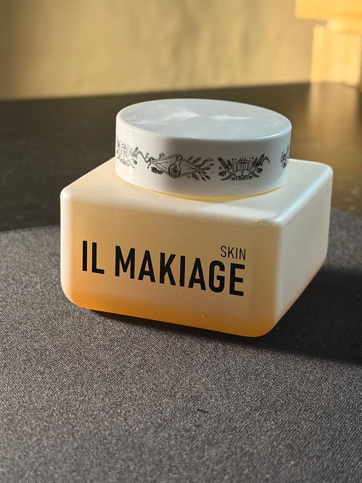 A square cream-colored cosmetic jar with a white lid, featuring the brand name 'IL MAKIAGE SKIN' printed in black on the front, set on a dark textured surface.