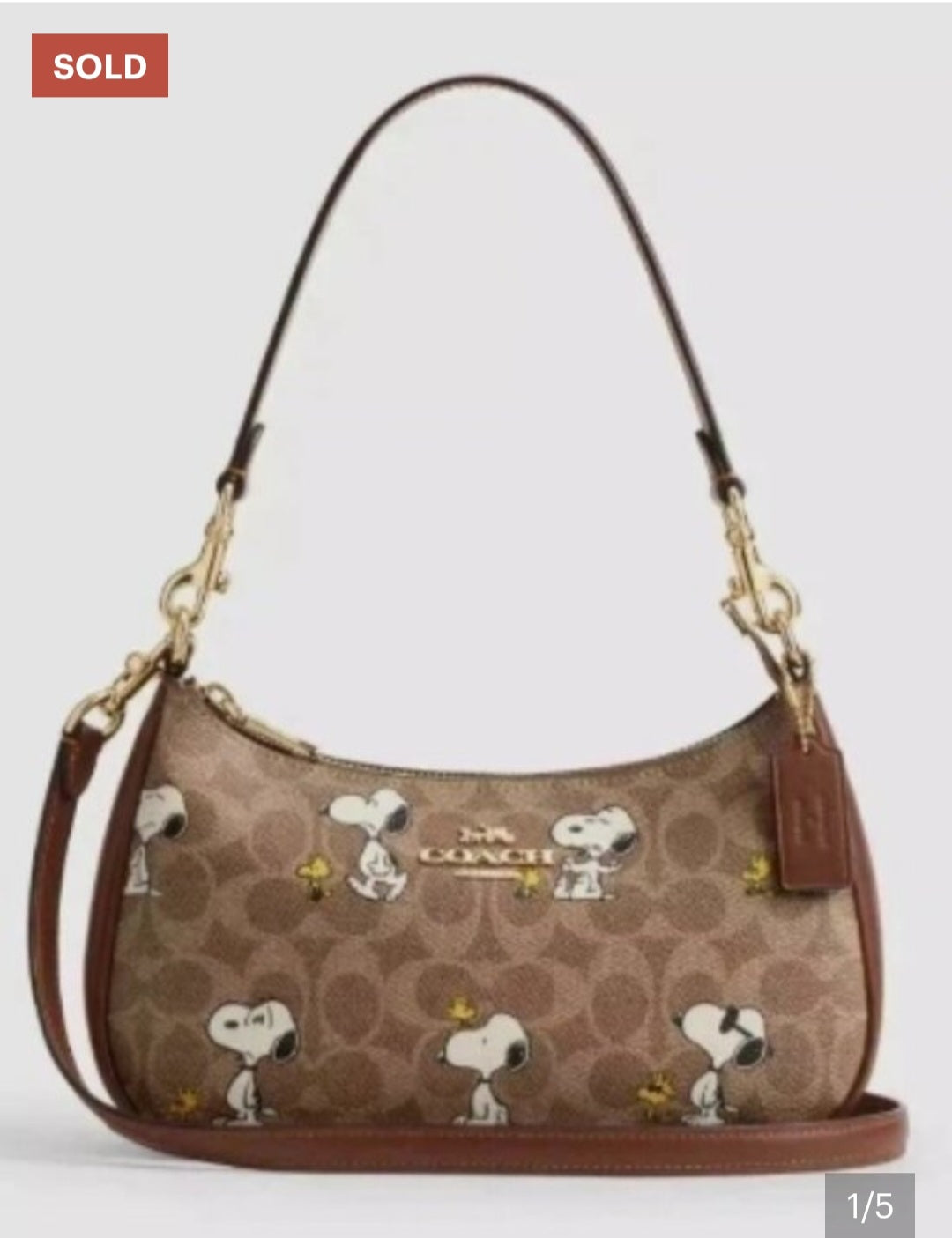 A Coach hobo shoulder bag in brown signature canvas with an all-over Snoopy and Woodstock print, featuring brown leather trim, gold-tone hardware, and a brown leather hangtag.