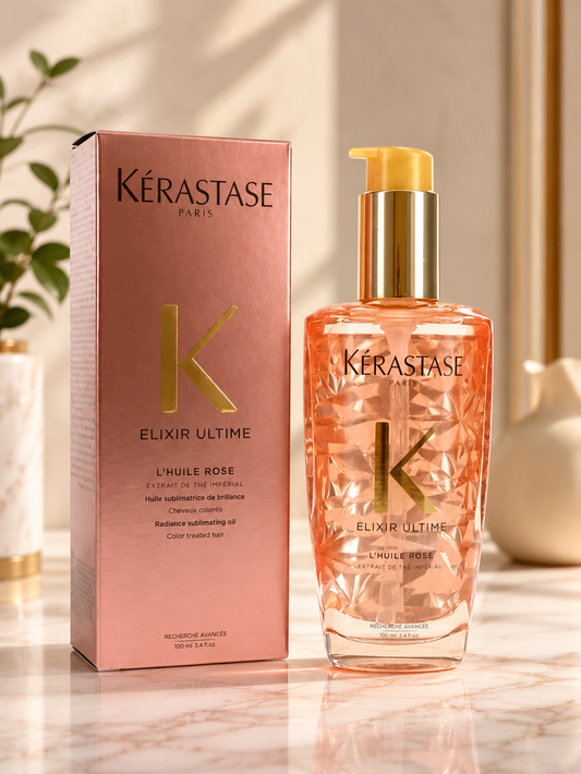 Kérastase Elixir Ultime Rose hair oil bottle with a gold pump next to its pink packaging box on a marble surface.