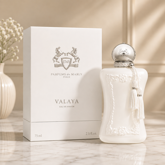 A white textured perfume bottle with a silver cap and tassel stands beside its white box, both printed with the brand name Valaya Parfums de Marly, on a marble surface with a soft beige background.